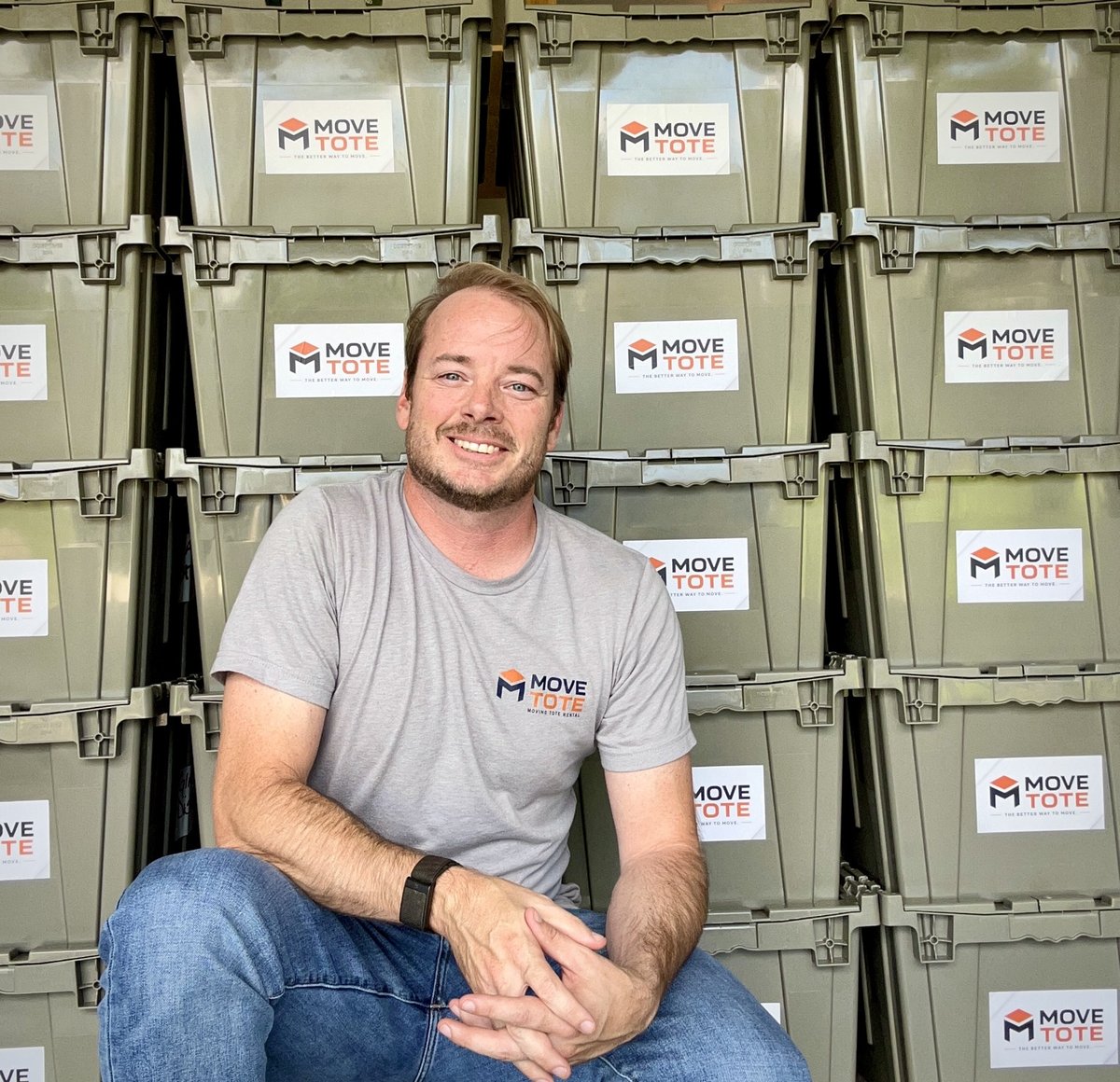 Evan, owner of MoveTote, seated in front of a wall of stacked moving totes